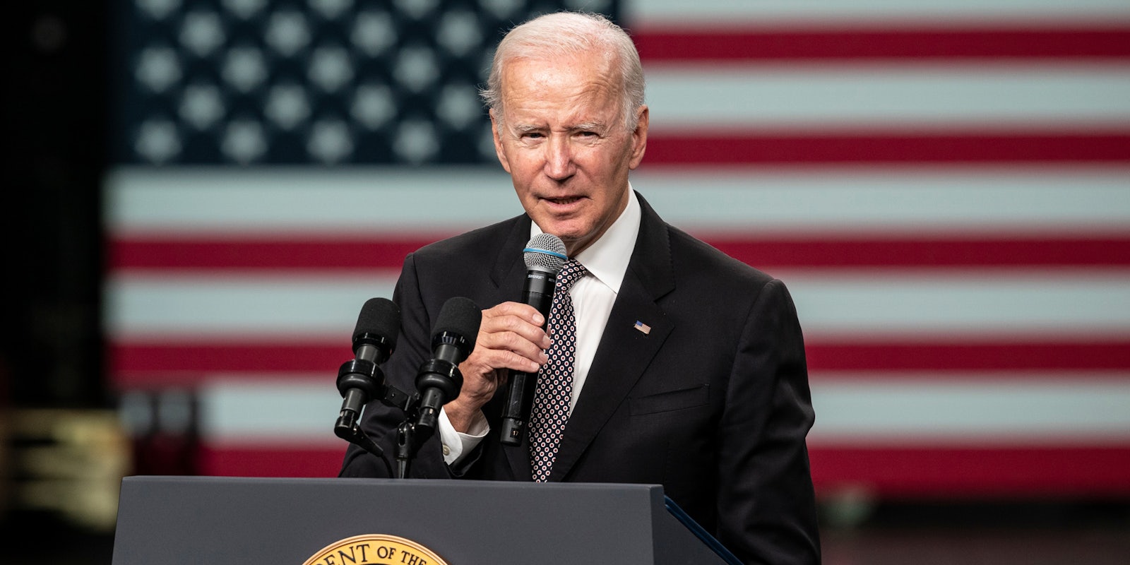 Joe Biden speaking into microphone at podium in front of American flag