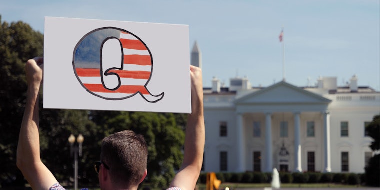 A man holds a 'Q' protest sign outside