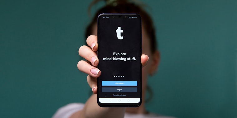 woman in front of green background holding phone with Tumblr on screen