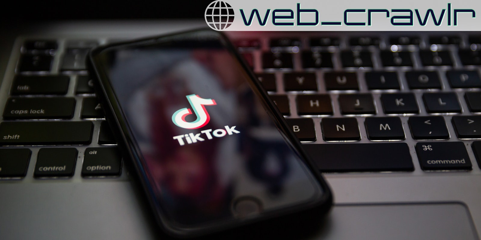 A phone with the TikTok logo on it sitting on a laptop. The Daily Dot newsletter web_crawlr logo is in the top right corner.