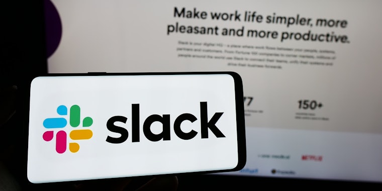 hand holding phone with Slack on screen in front of computer screen with Slack website