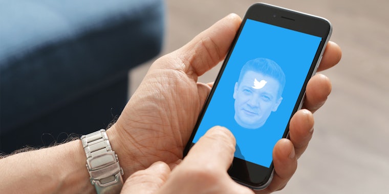 man holding phone with Twitter and Jeremy renner on screen in front of blurred living room background