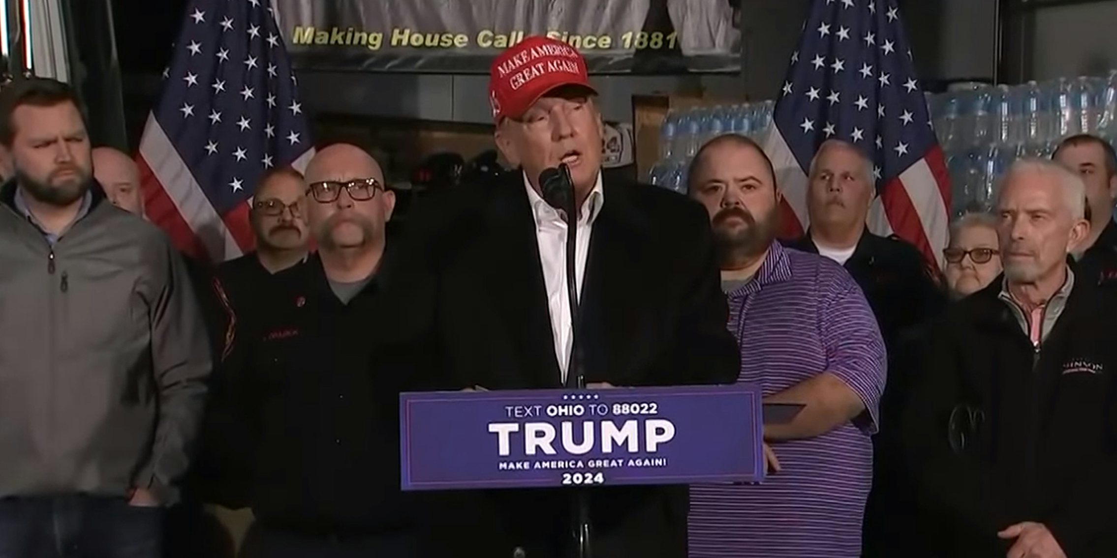 Donald Trump speaking into microphone in front of group of people in front of bottled water