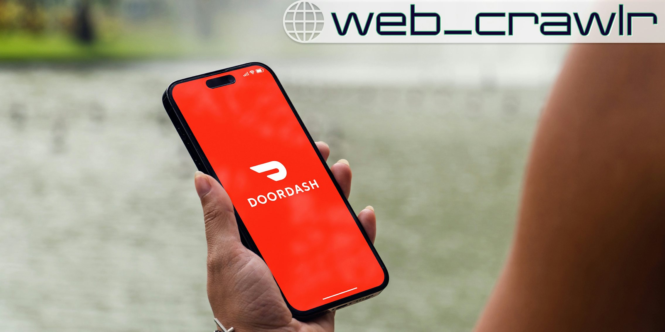 A person holding a phone with the DoorDash logo on it. The Daily Dot newsletter web_crawlr logo is in the top right corner.