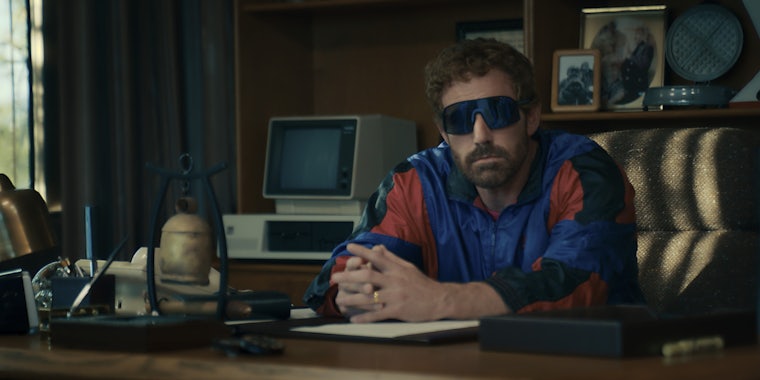 Ben Affleck wearing large sunglasses and a tracksuit sitting at a desk in the new movie AIR.