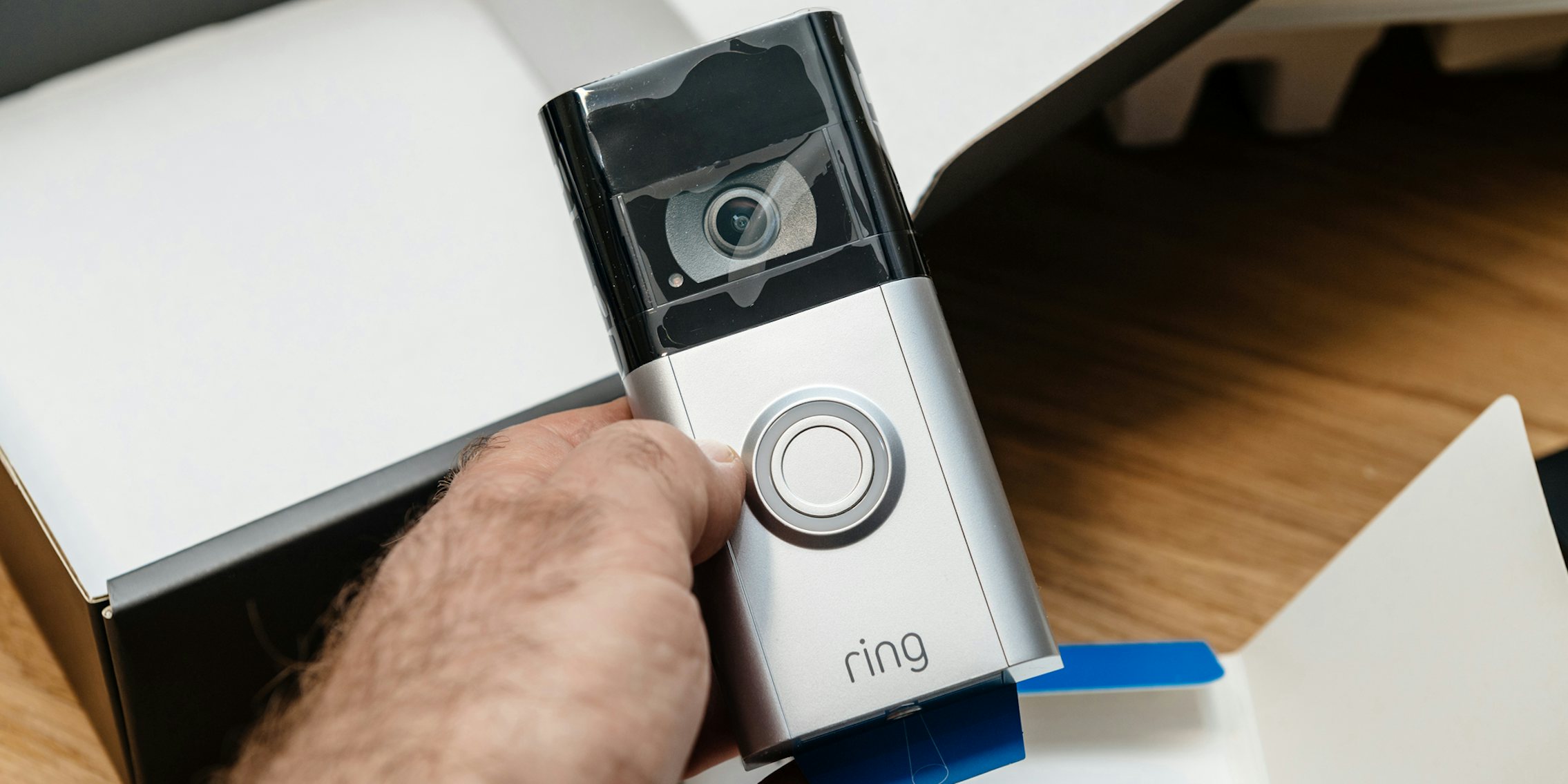 Amazon Ring camera in hand in front of packaging on wooden surface