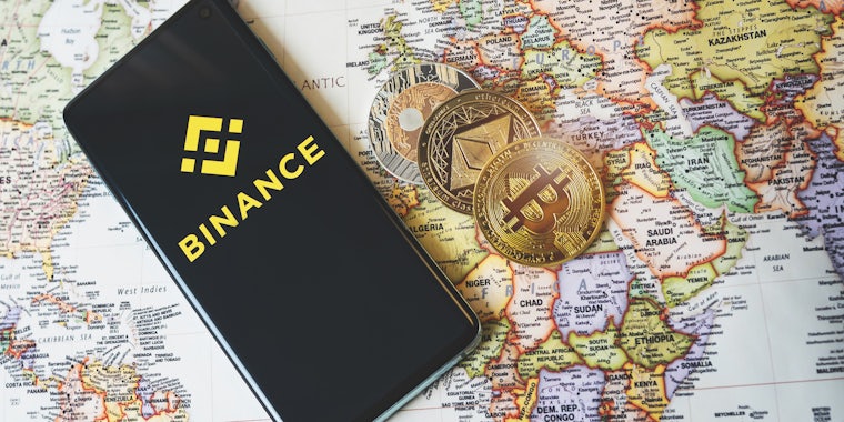 Binance app logo on a smartphone and crypto coins Bitcoin, Ethereum and XRP on a world map.