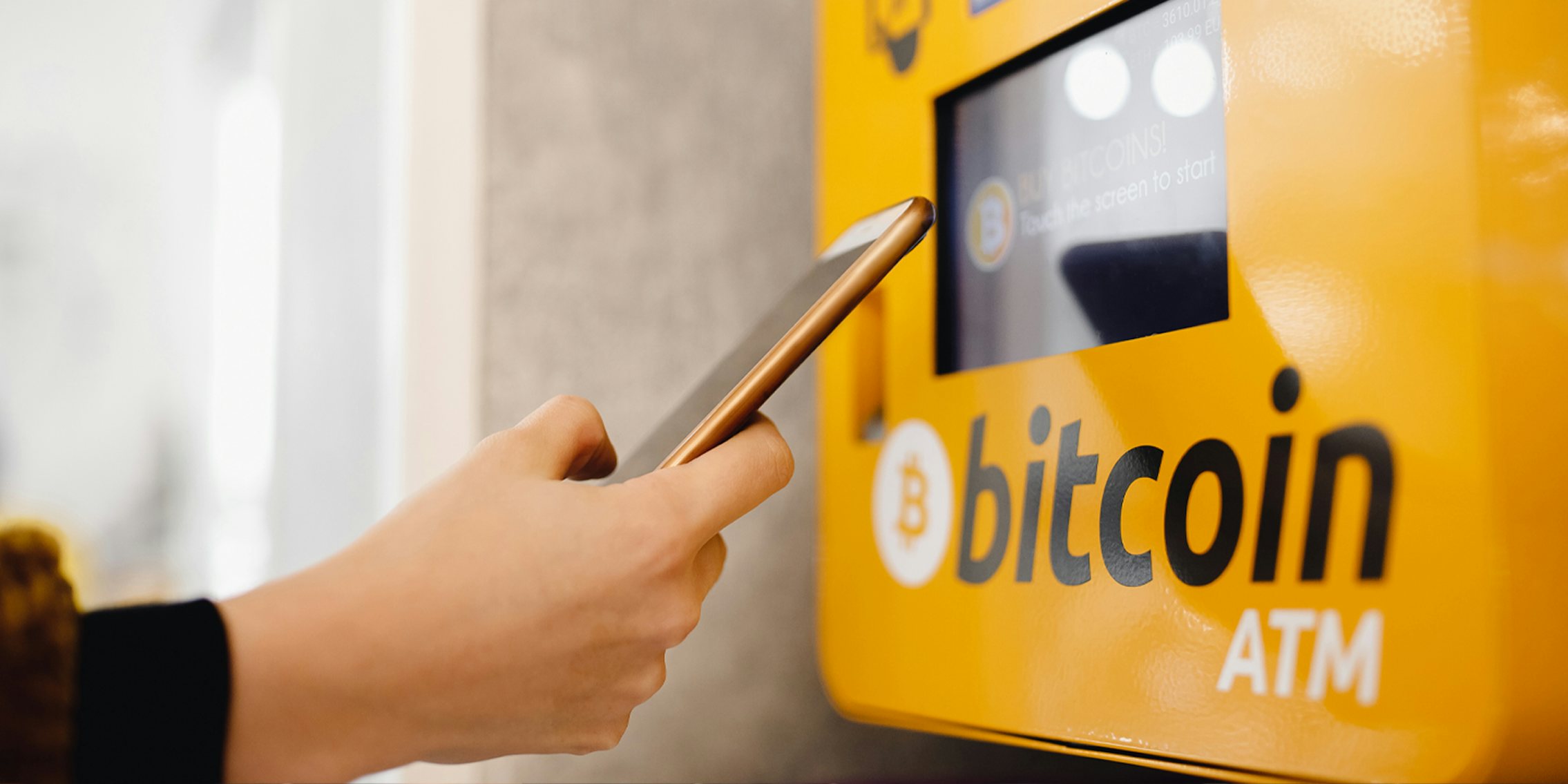 hand with phone up to Bitcoin ATM