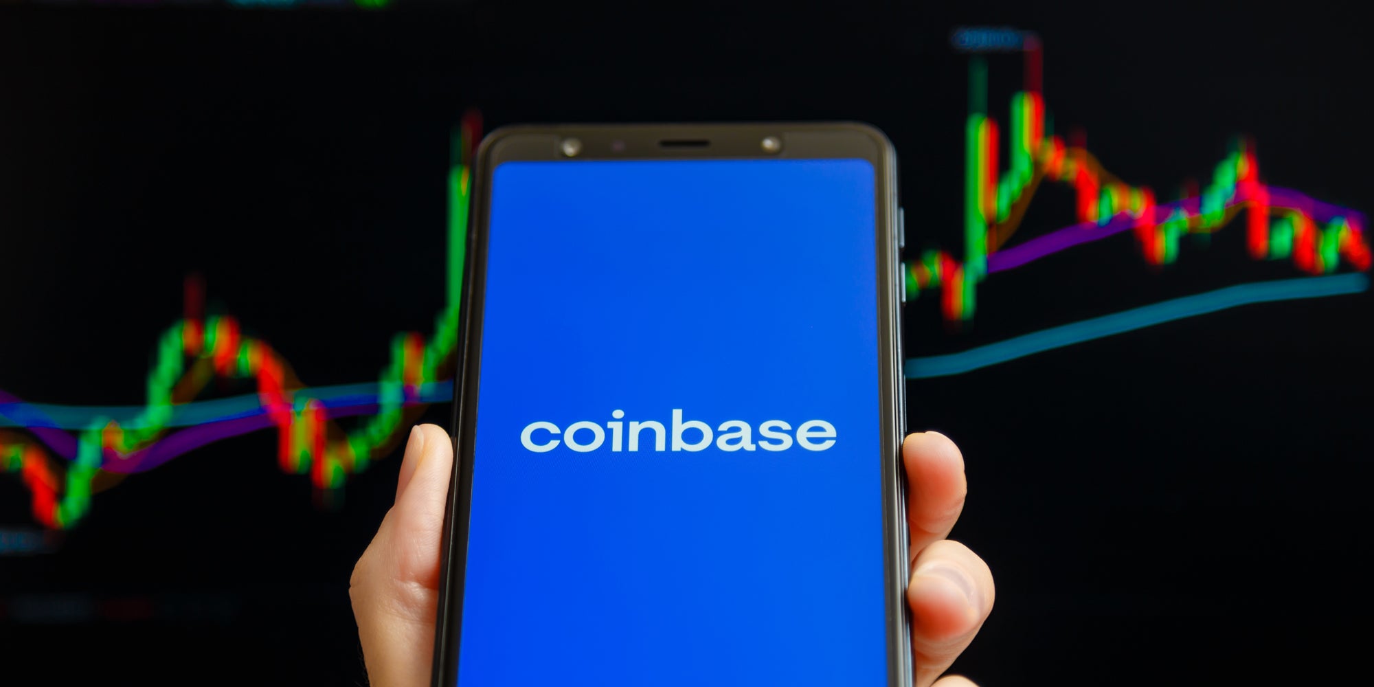 Coinbase on phone in hand in front of chart black background