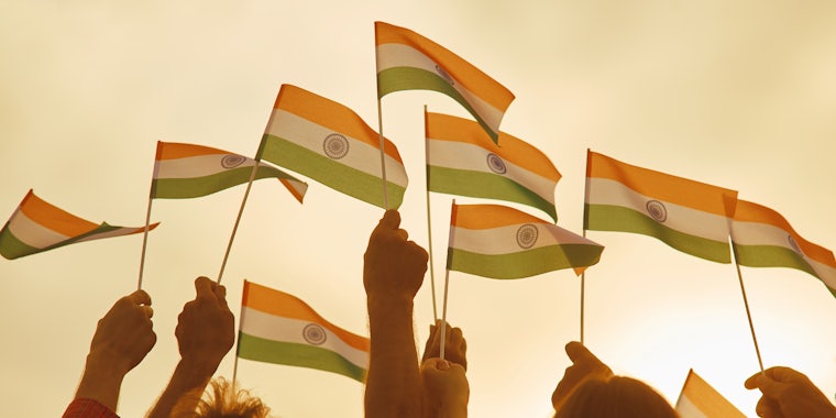 group of people holding up miniature Indian flags in front of light yellow background