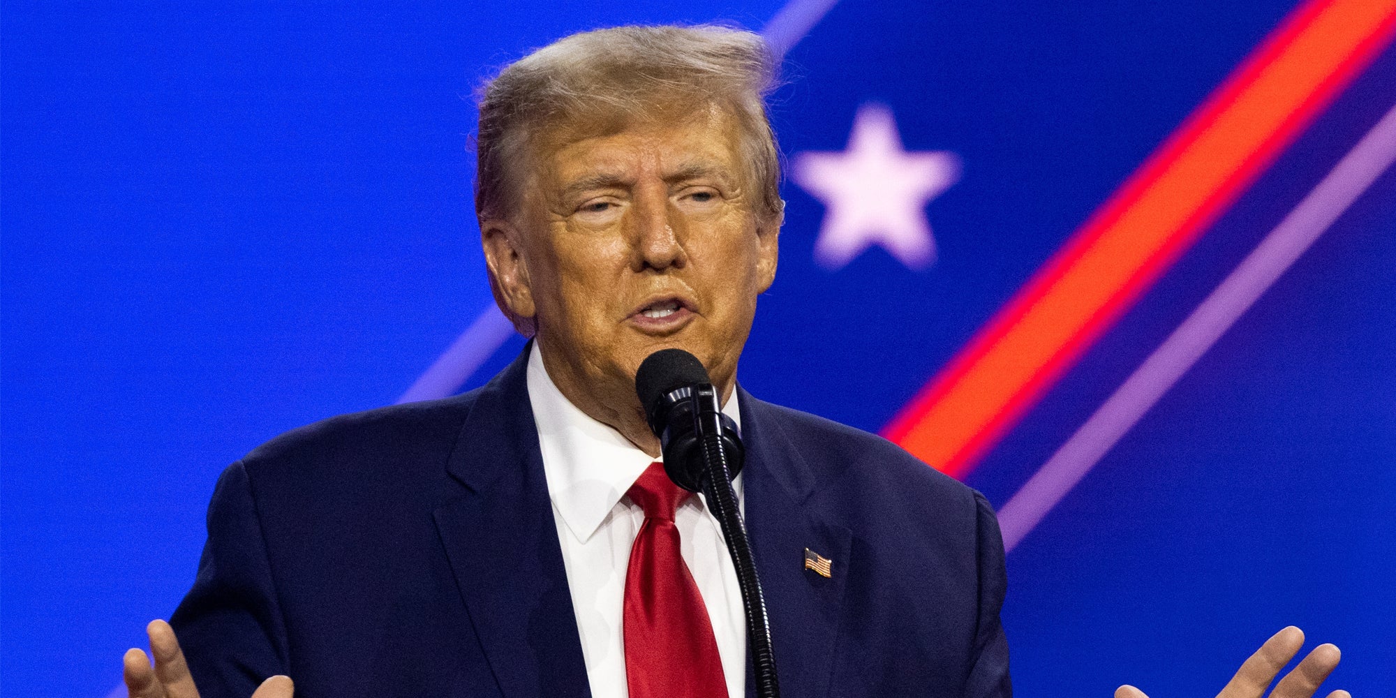 Donald Trump speaking into microphone in front of blue background