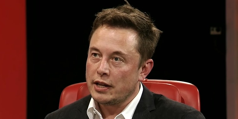 Elon Musk speaking in red chair in front of black and red background