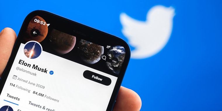 Elon Musk Twitter account on phone screen in front of Twitter blurred background