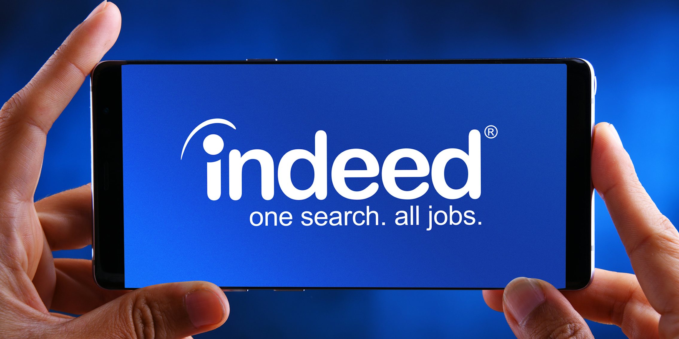 Indeed job search app on phone in hands in front of blue background