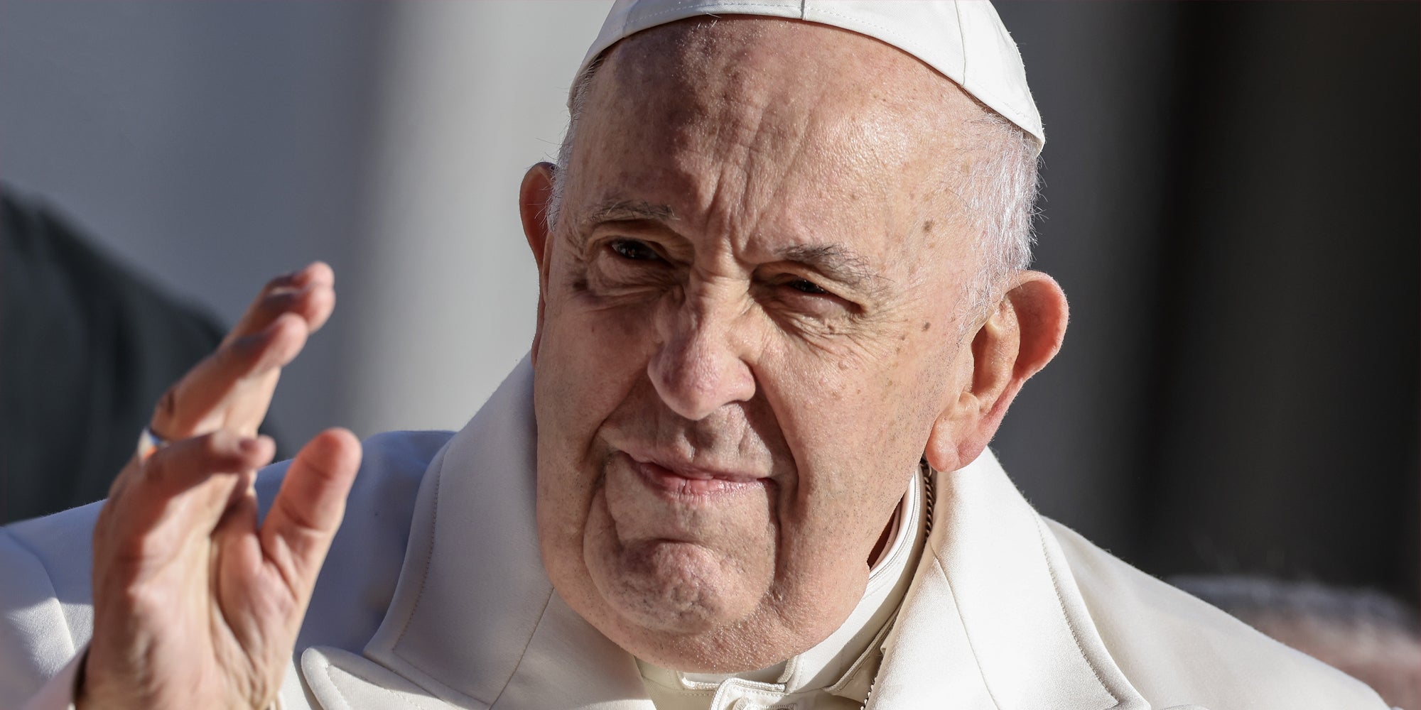 Pope Francis with hand up in front of blurry grey background