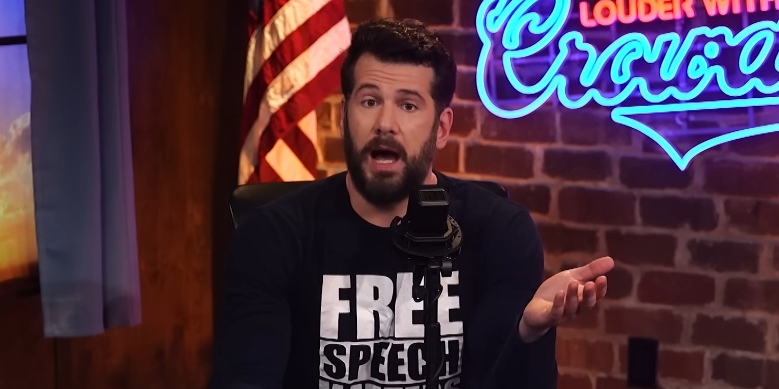 Steven Crowder speaking into microphone in front of brick background