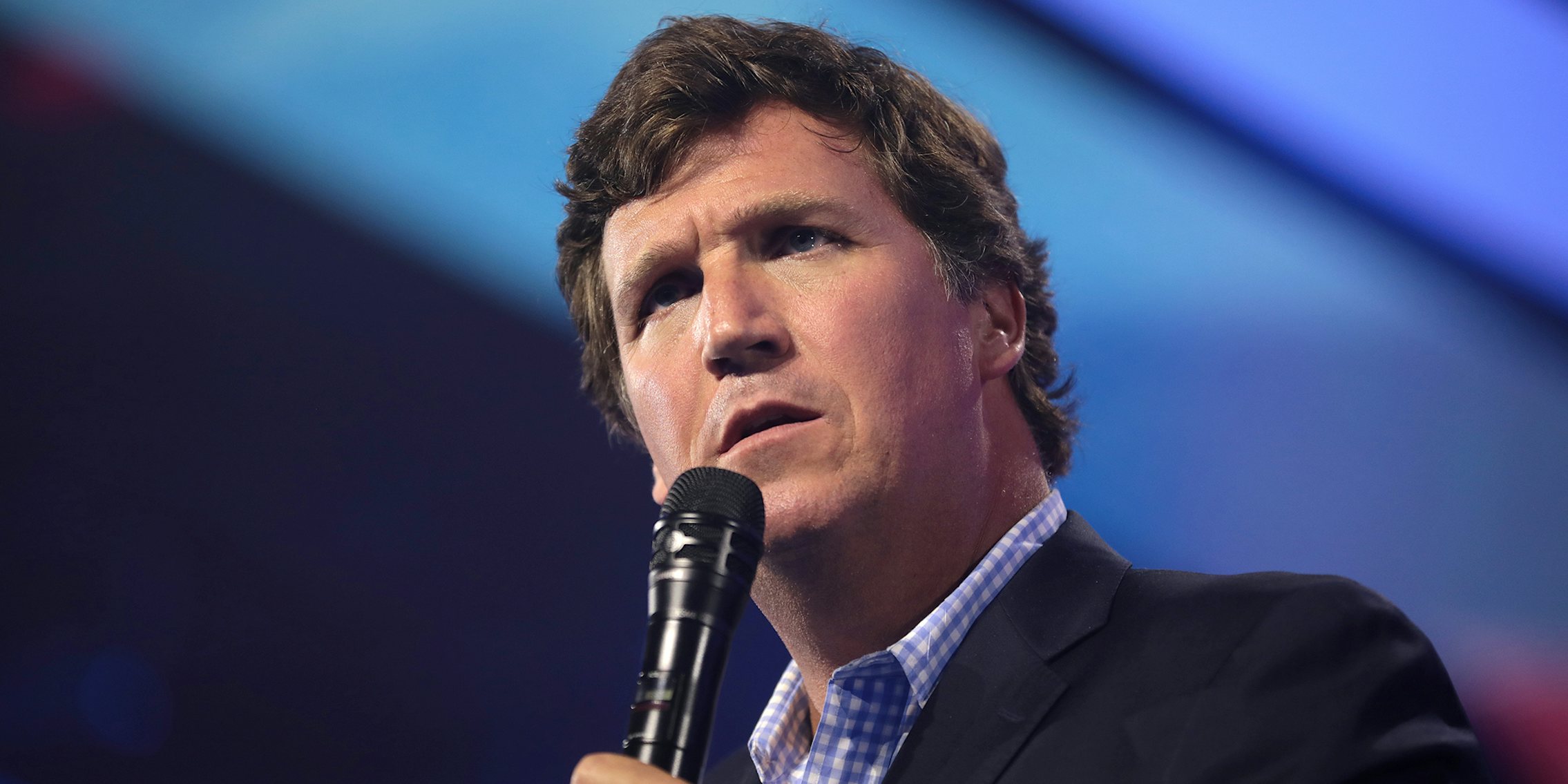 Tucker Carlson speaking into microphone in front of blue background