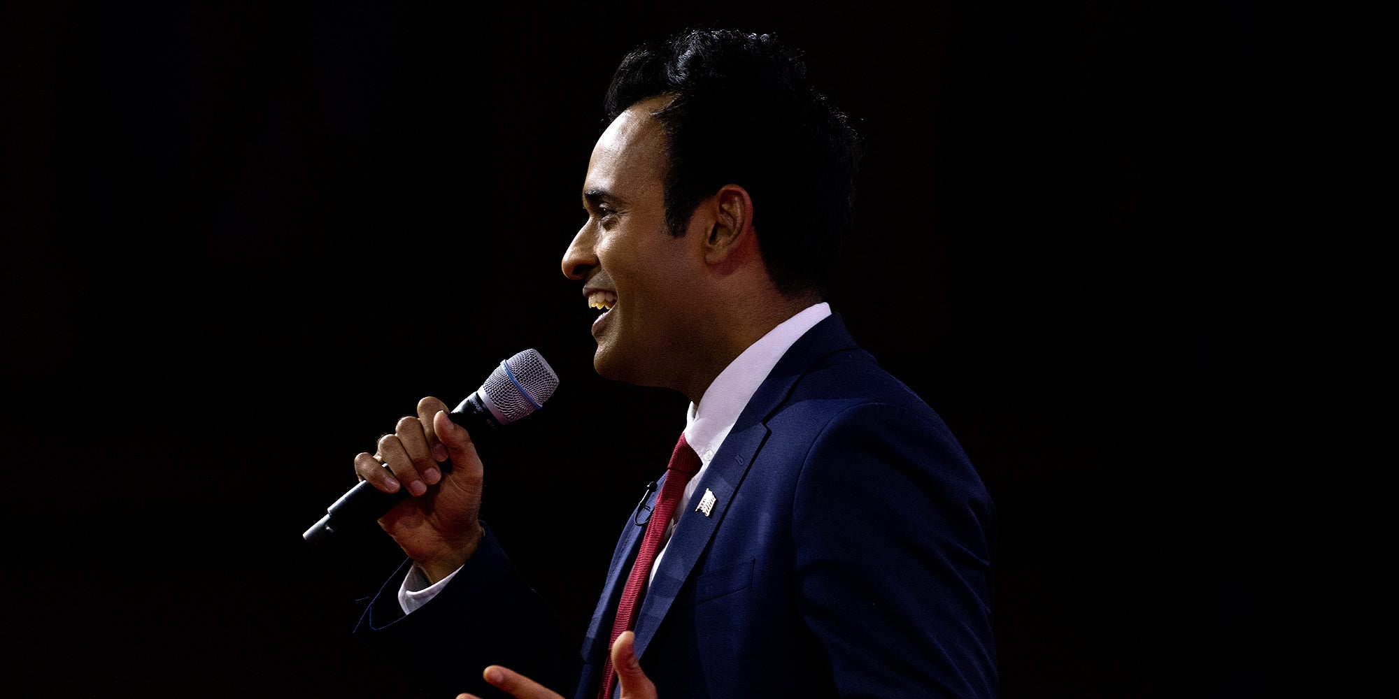 Vivek Ramaswamy speaking into microphone in front of black background