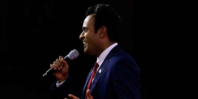 Vivek Ramaswamy speaking into microphone in front of black background