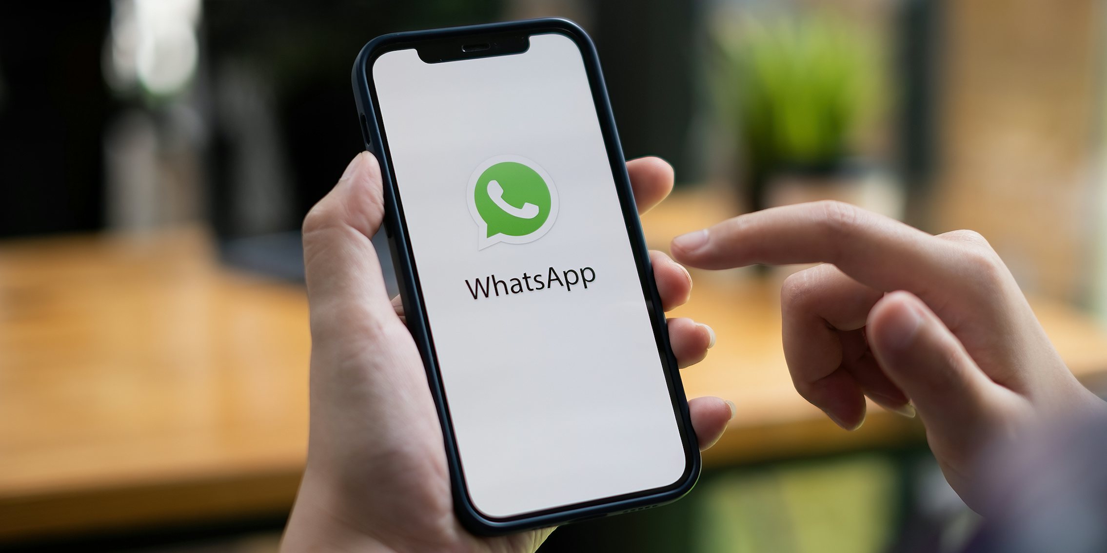 WhatsApp on phone screen in hand in front of blurry desk background