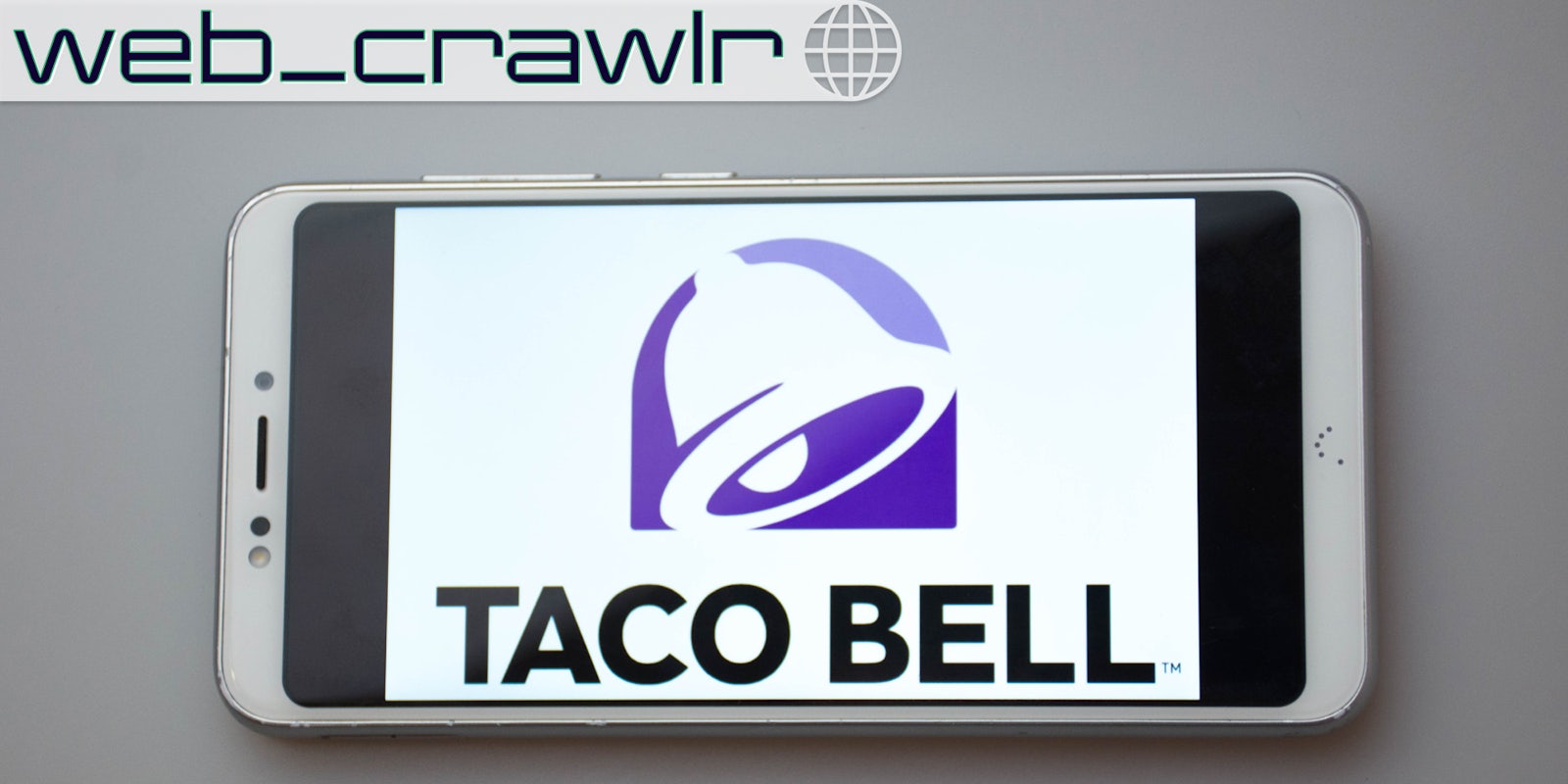 A phone showing the Taco Bell logo on it. The Daily Dot newsletter web_crawlr logo is in the top left corner.