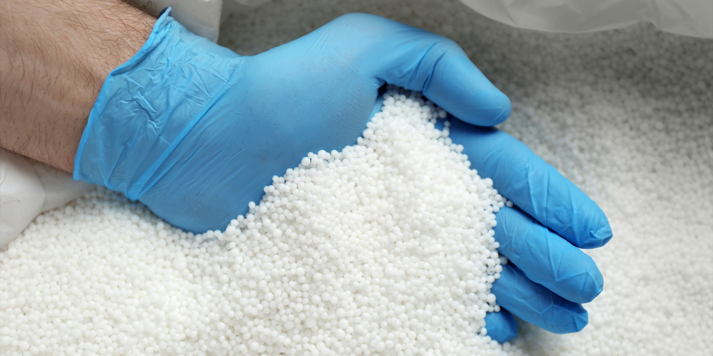hand in blue glove taking pellets of ammonium nitrate from bag
