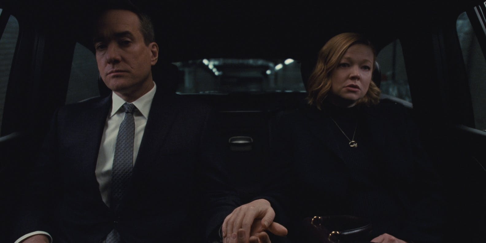 a man in a suit sitting next to a woman in a car, with her hand in his. One of the final shots in the HBO series Succession