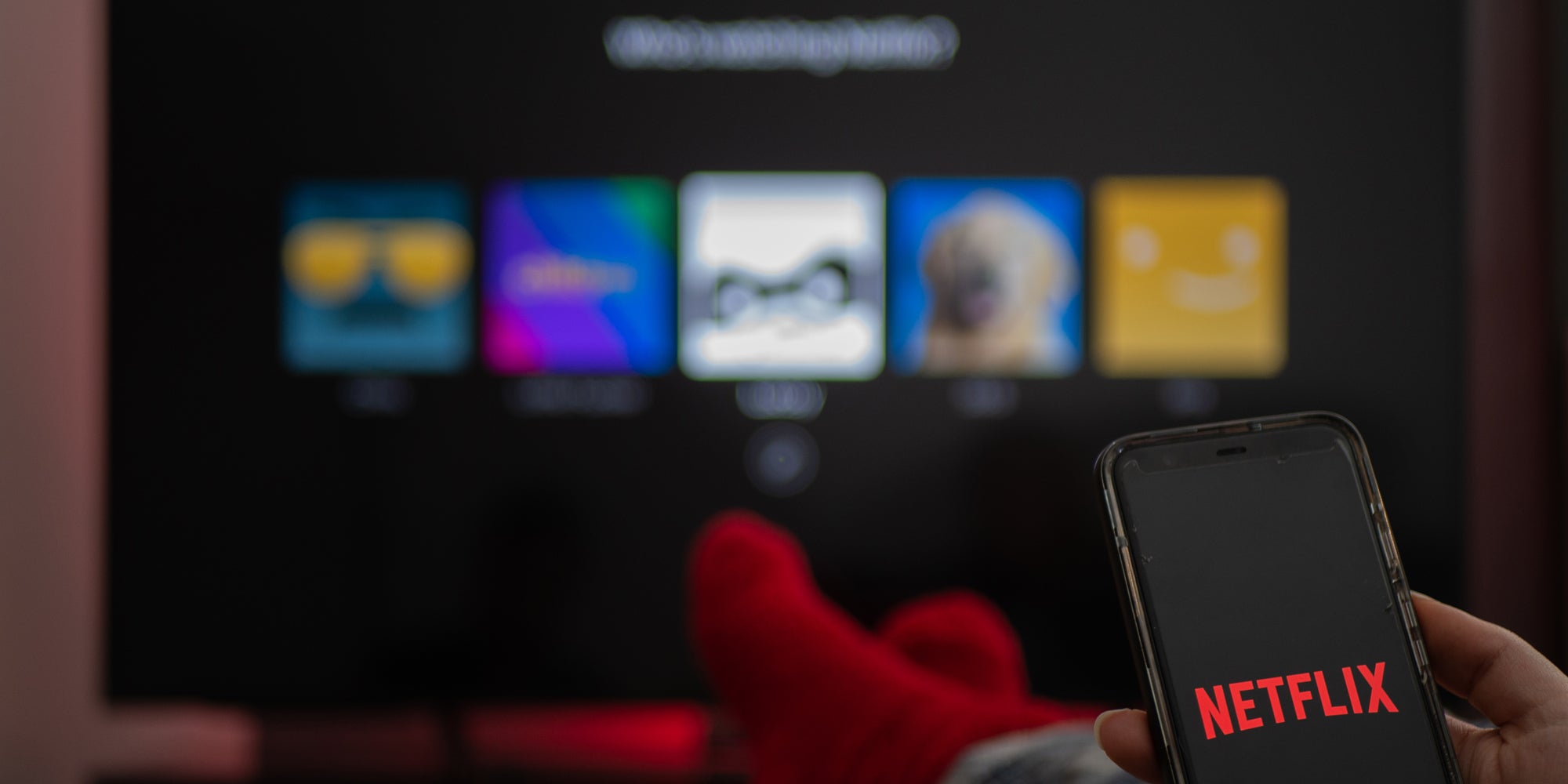 Netflix on tv blurred behind phone in hand with Netflix on screen