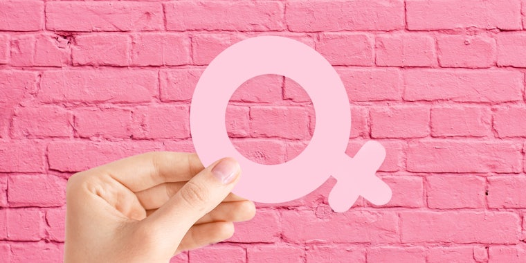 hand holding female symbol in front of pink bricks background