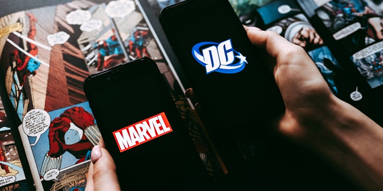 hands holding the iPhone with Marvel and DC comics logo on the screen. comics page background.