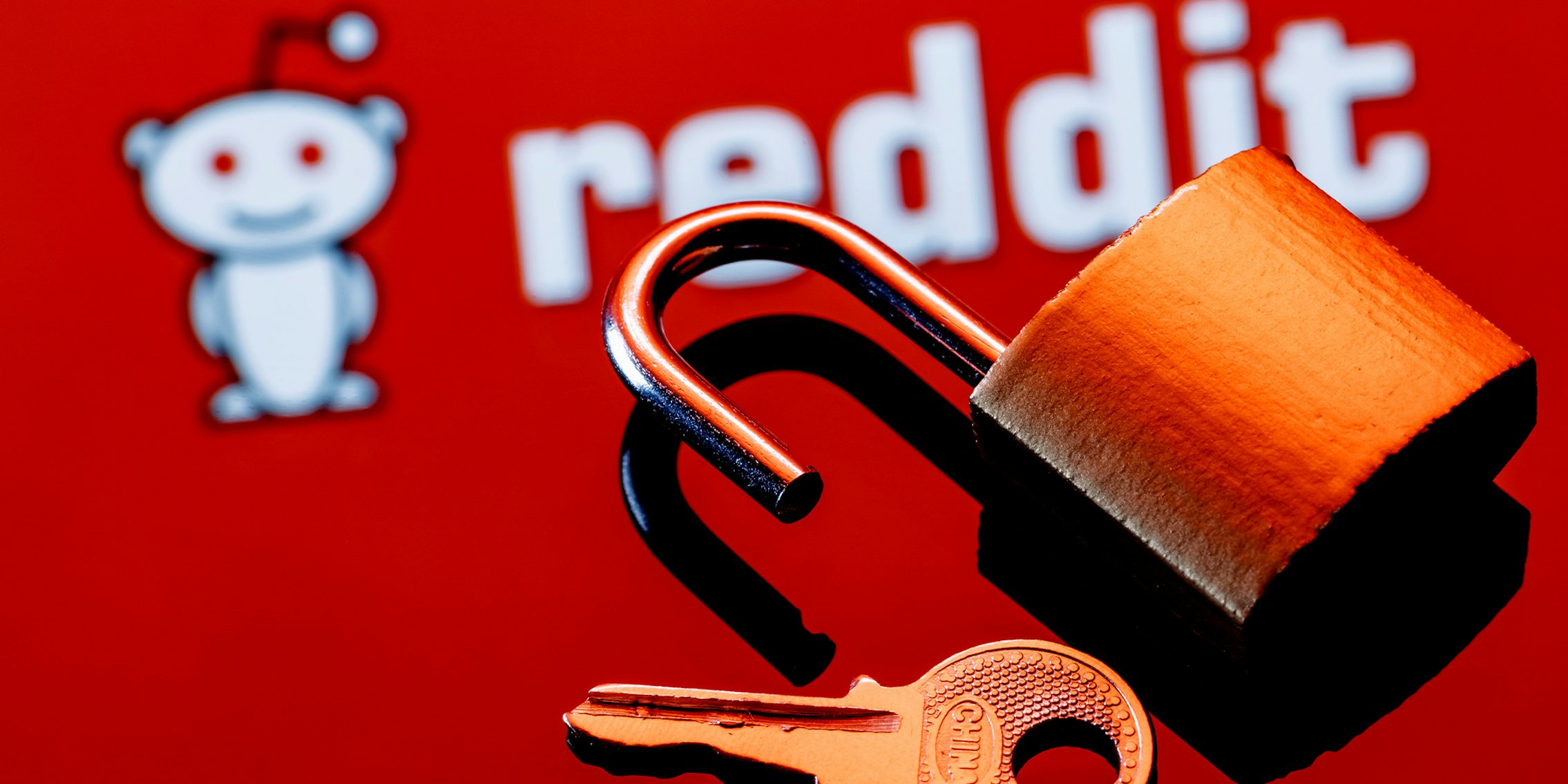 Hackers blackmail Reddit over third-party app plans; An open security lock and key on the background of the Reddit discussion platform logo in the mirror reflection.