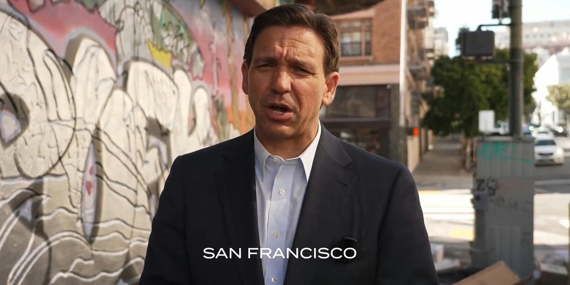Ron DeSantis speaking on sidewalk in town with caption "San Francisco"