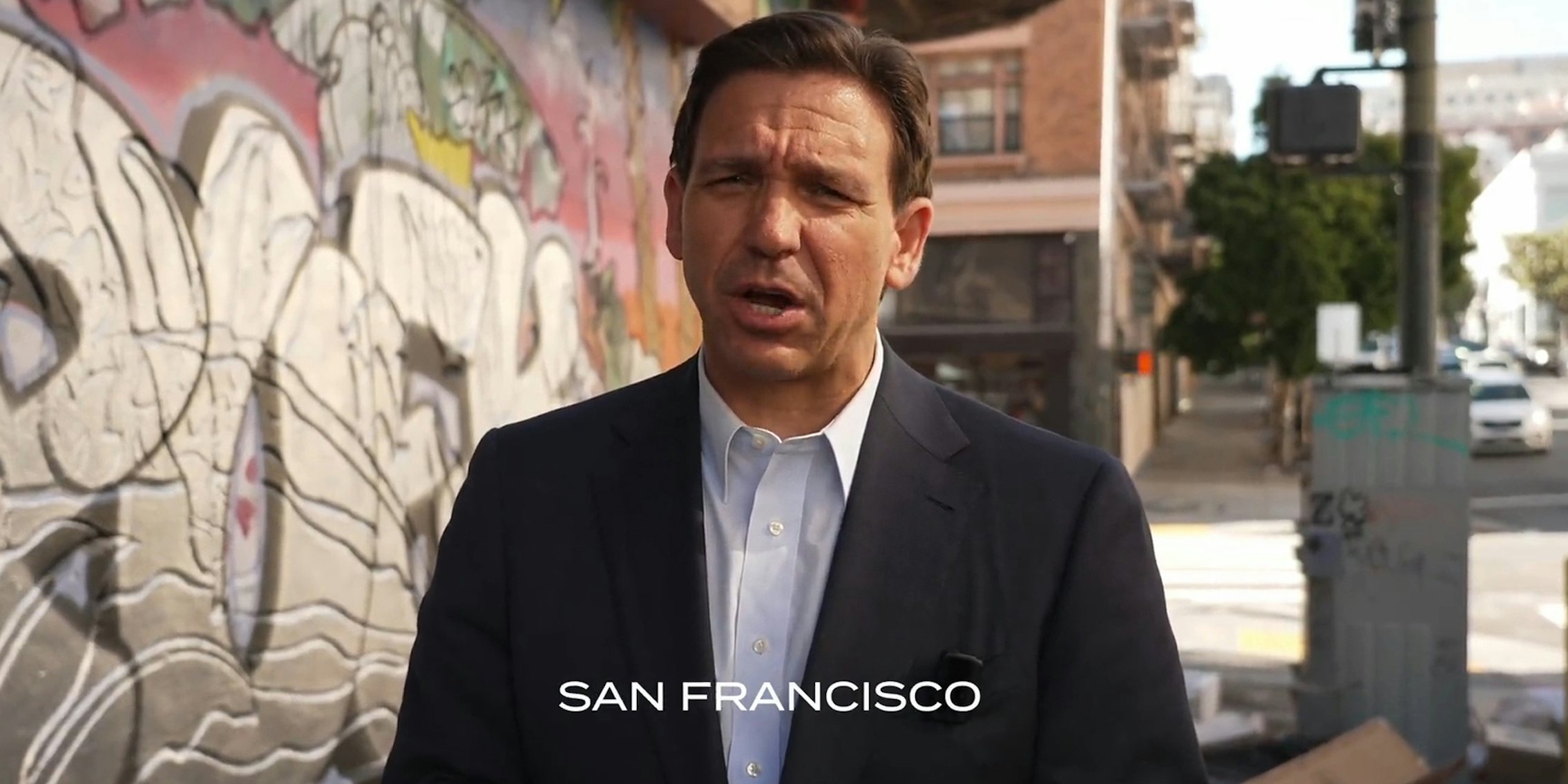 Ron DeSantis speaking on sidewalk in town with caption 'San Francisco'