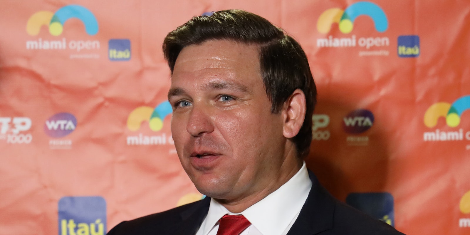 Ron DeSantis speaking in front of coral colored background