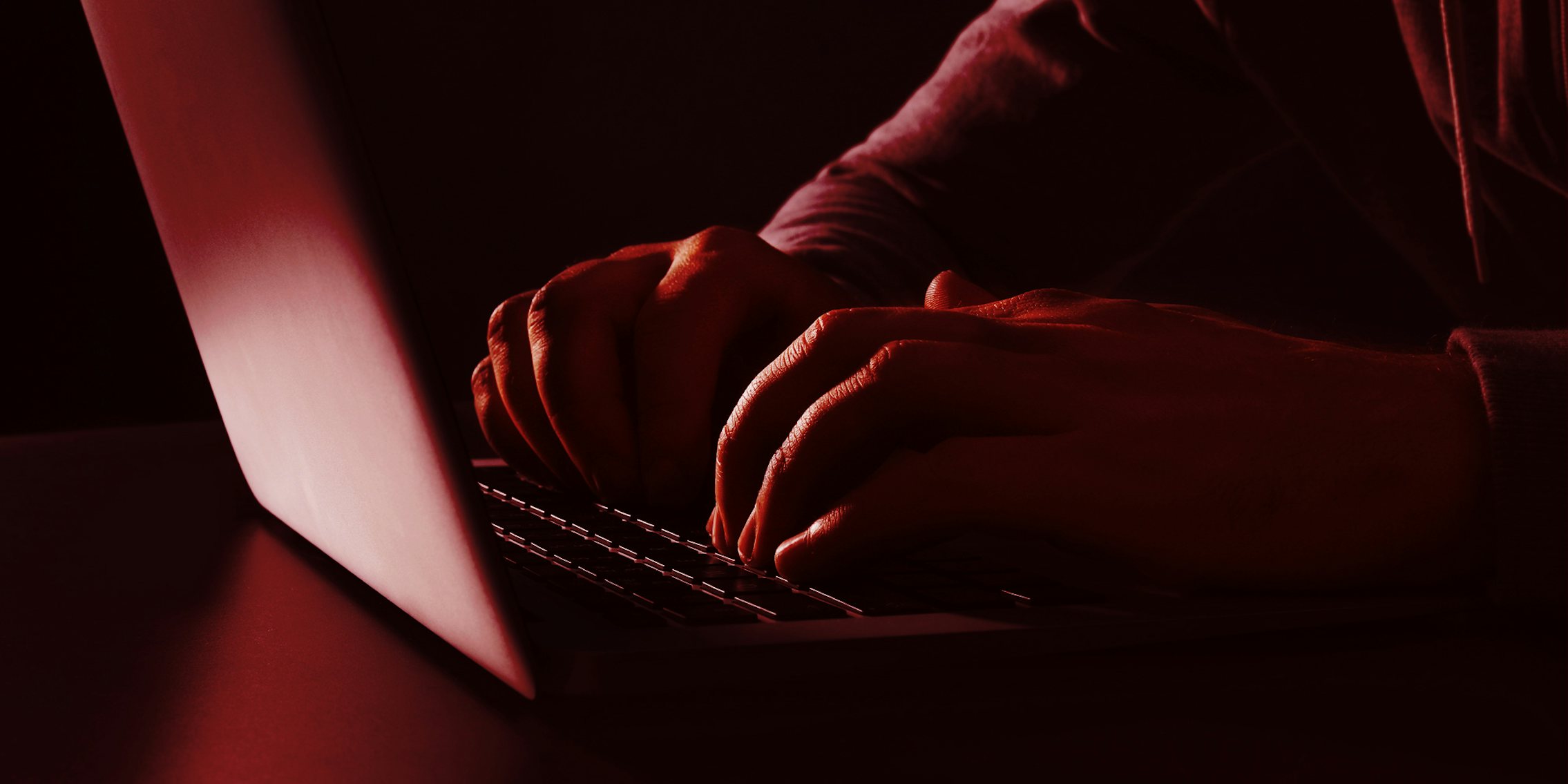man in hoodie typing on laptop with red overlay