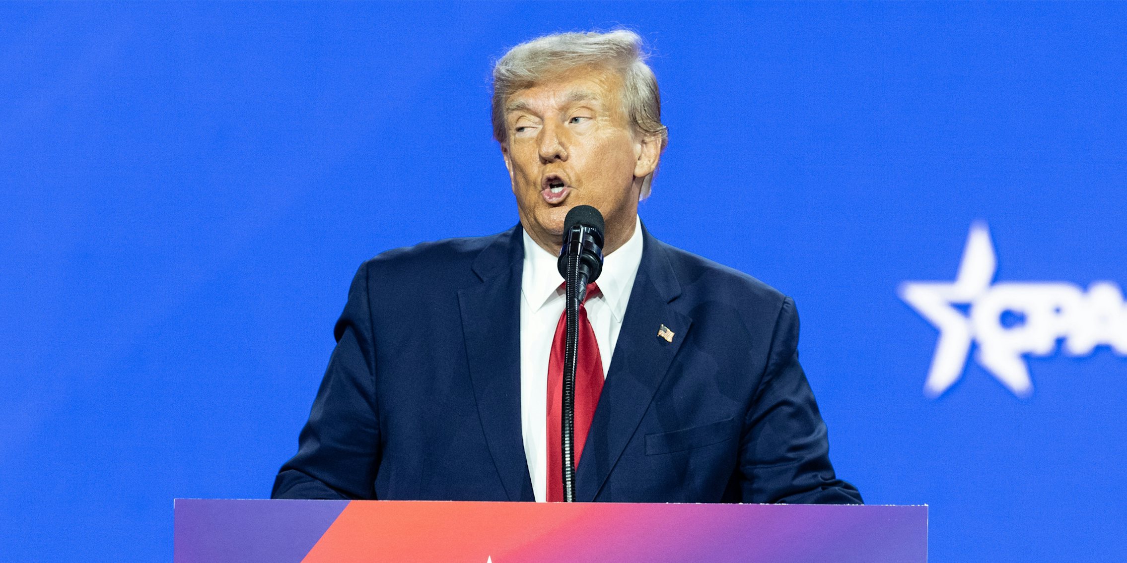 Donald Trump speaking into microphone in front of blue background