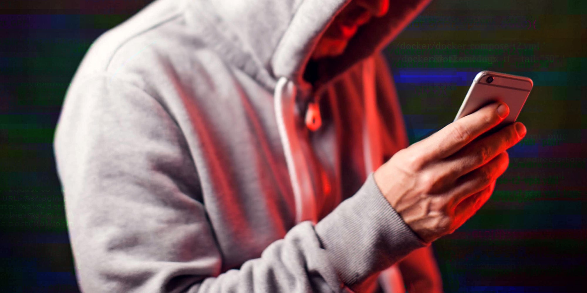 man in hoodie holding red lit phone in front of abstract glitched code background
