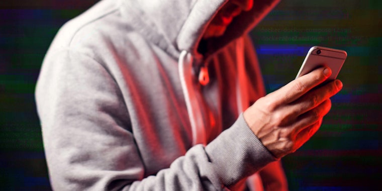 man in hoodie holding red lit phone in front of abstract glitched code background