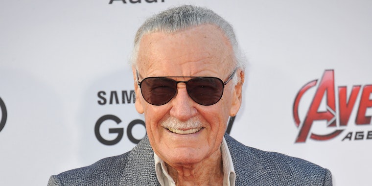 Stan Lee smiling in front of white Avengers background