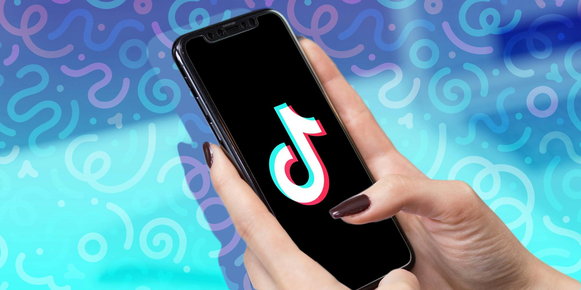 Two hands hold an iPhone displaying the TikTok logo in front of a multi-colored backdrop.