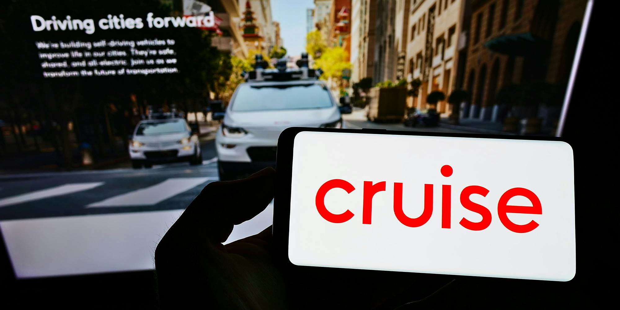 Person holding smartphone with logo of US self-driving car company Cruise LLC on screen in front of website