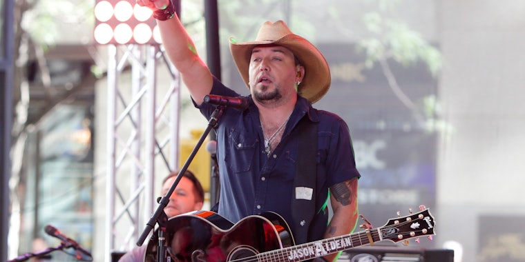 Jason Aldean singing into microphone on stage while holding guitar