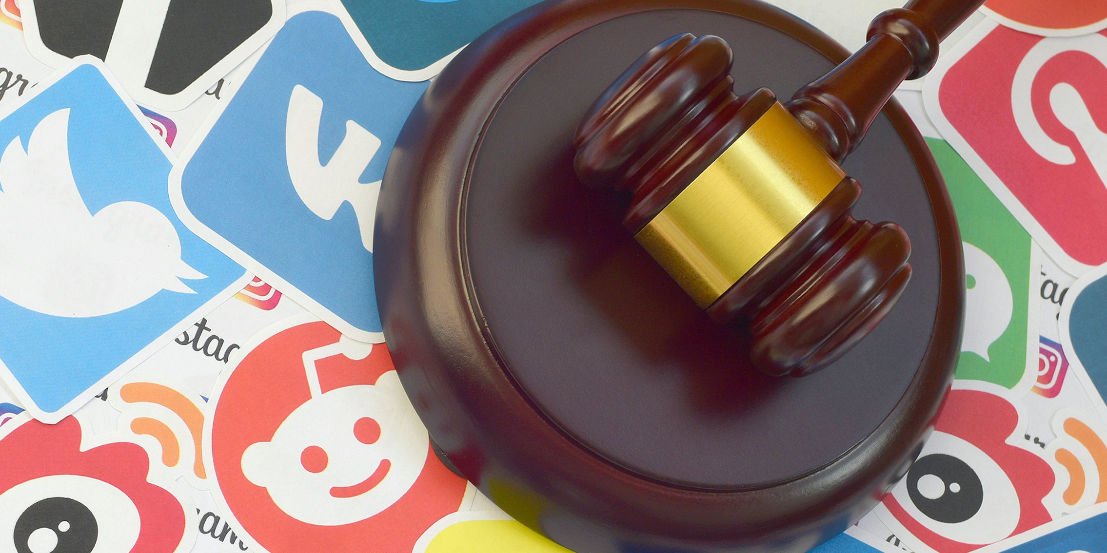 Wooden judge gavel lies on many paper logos of popular social network