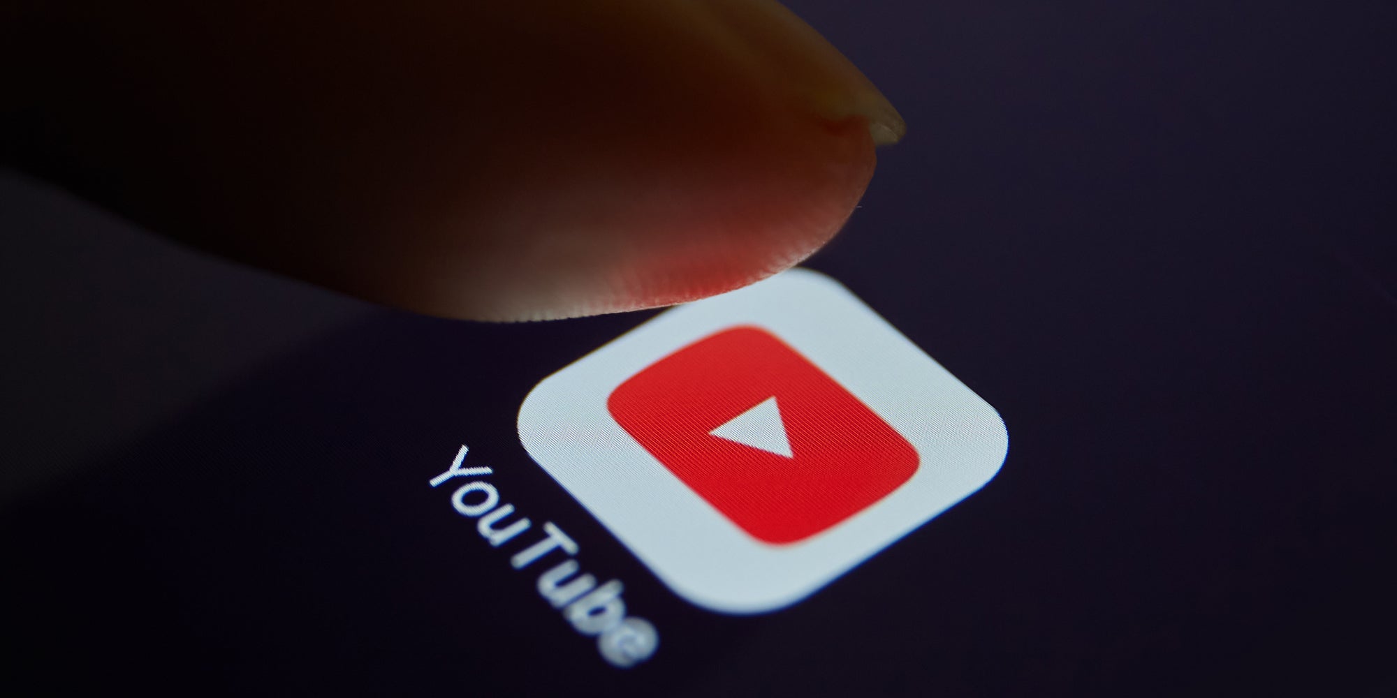 A person's finger above a YouTube app icon.