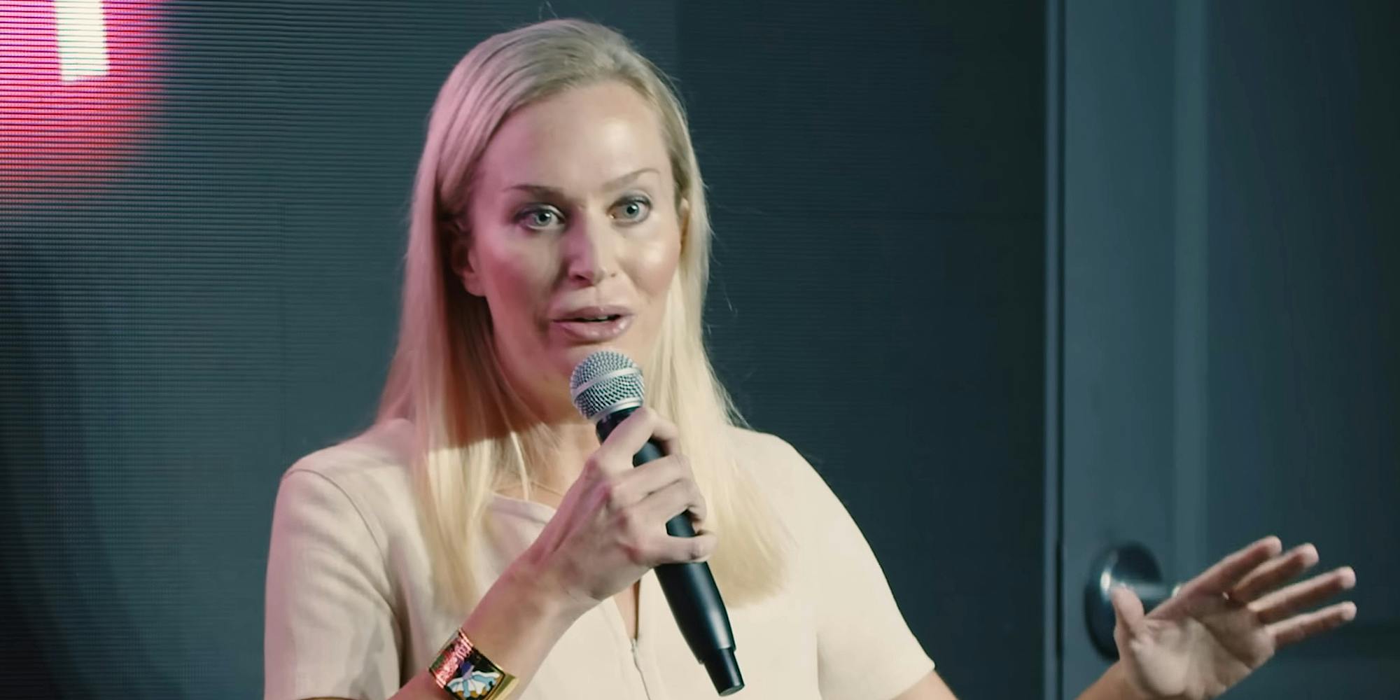 Christina Pushaw speaking into microphone in front of cyan background