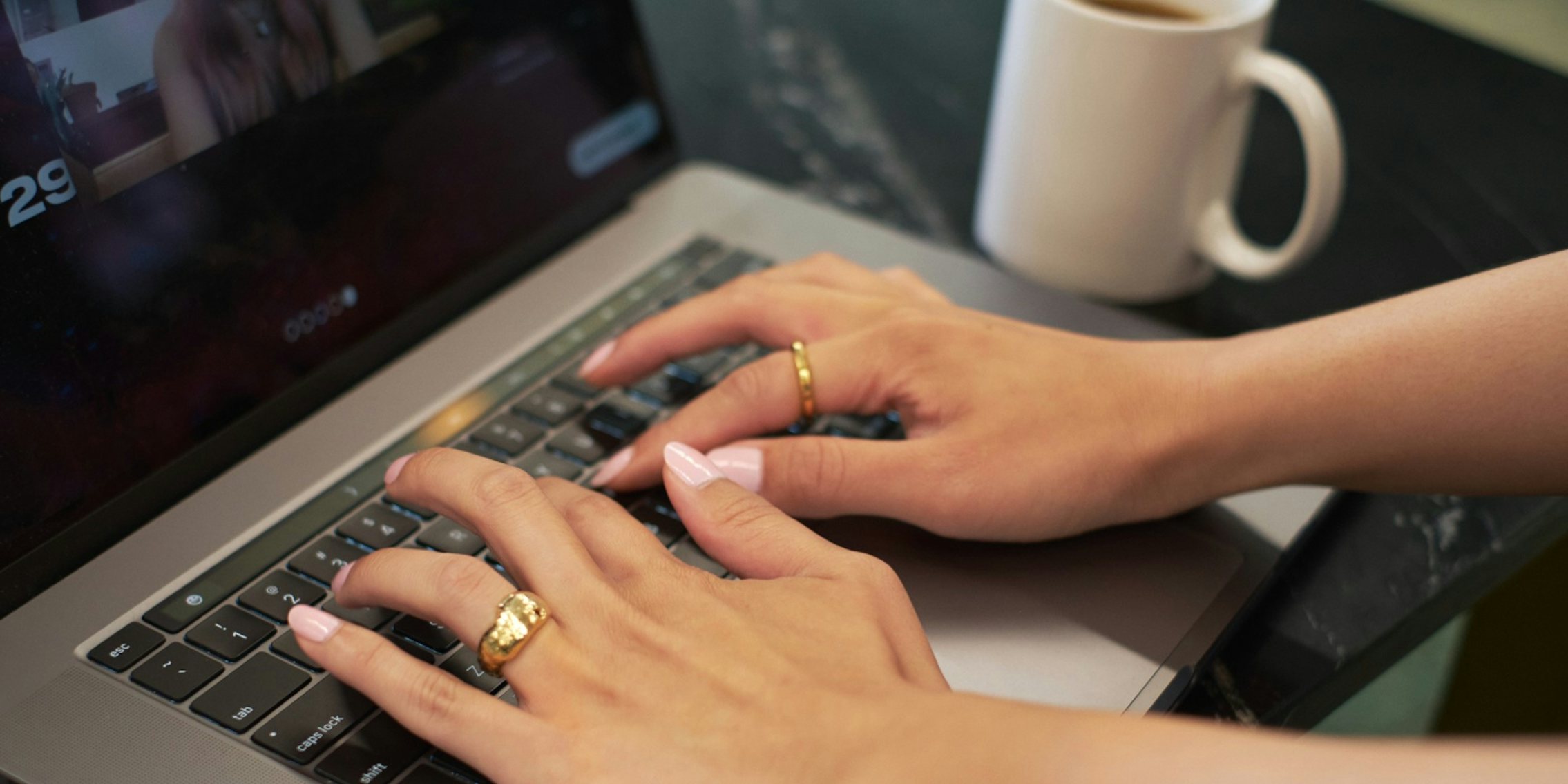 Person's hands with pink nails and rings typing on laptop