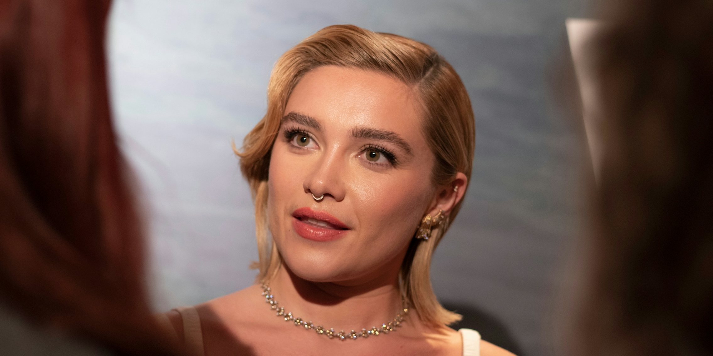 Florence Pugh with blonde hair and necklace looking at a person and talking to them. The actress stars in the new film Oppenheimer.