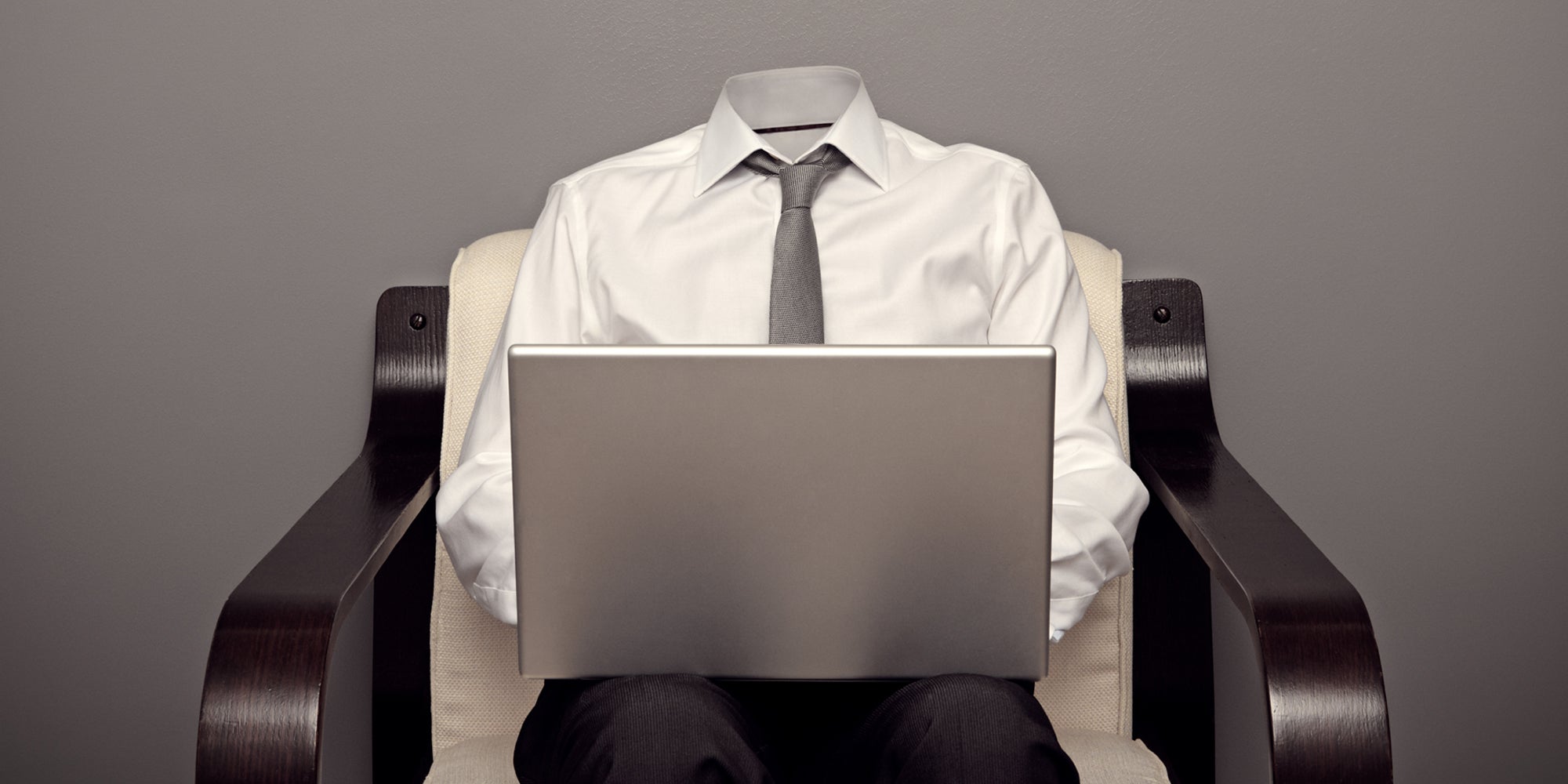 headless business man with laptop in chair in front of grey wall