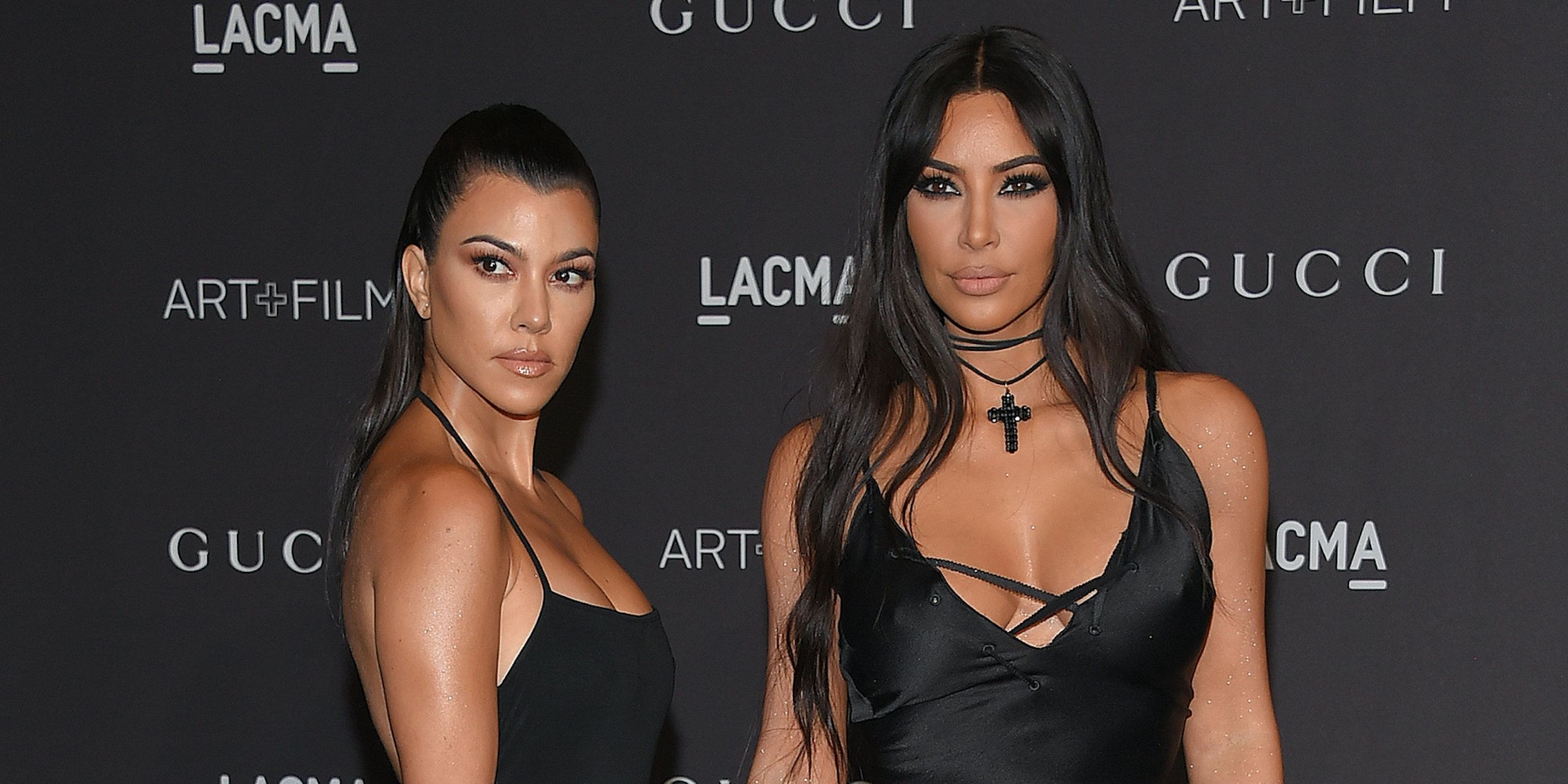 Kourtney Kardashian and Kim Kardashian in front of grey background