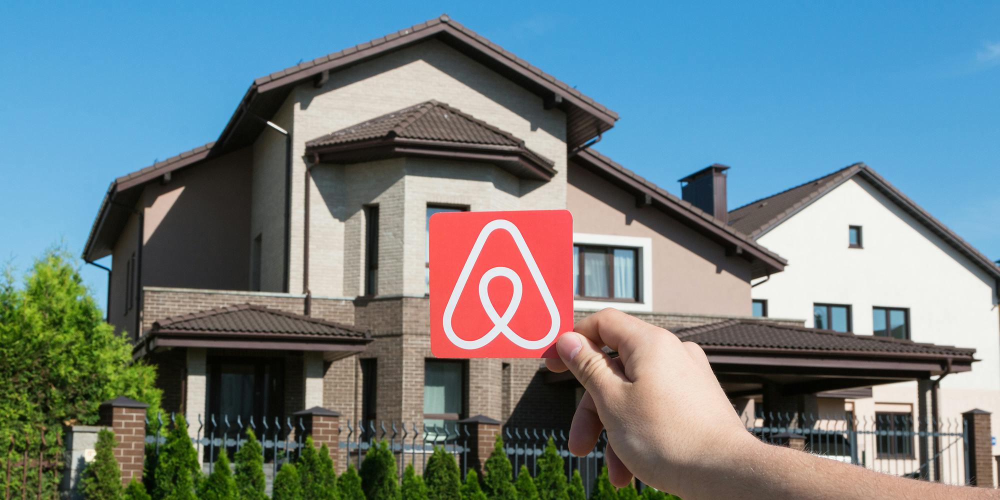 hand holding Airbnb logo on paper in front of house